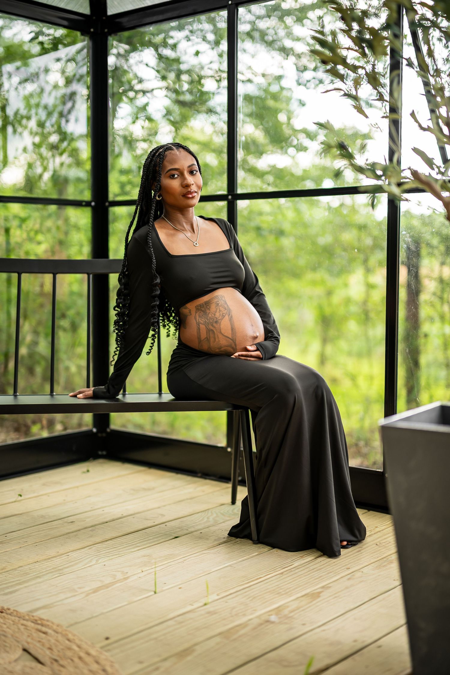 Maternity photography in a sunlit greenhouse with wooden flooring and glass walls.