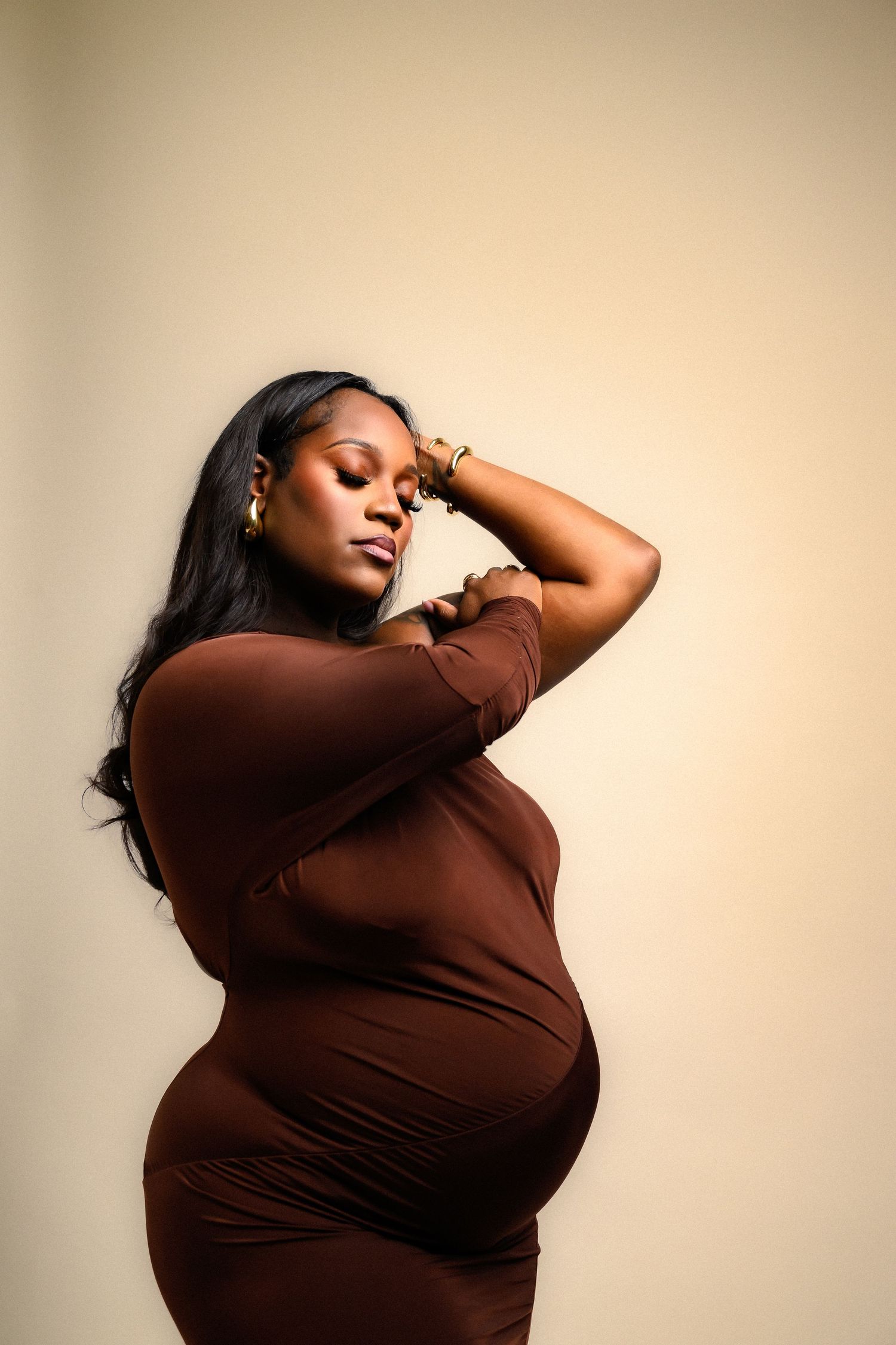 Artistic maternity self portraits in brown dress with dramatic poses against beige background.