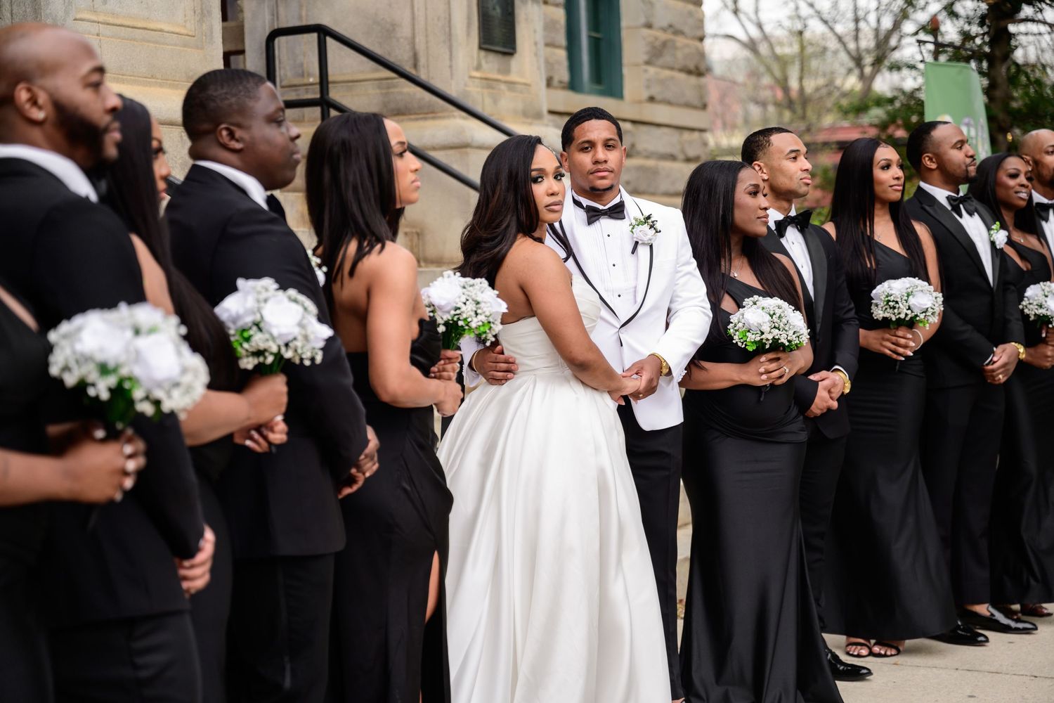 Wedding party in black and white attire poses on stone steps of historic building.