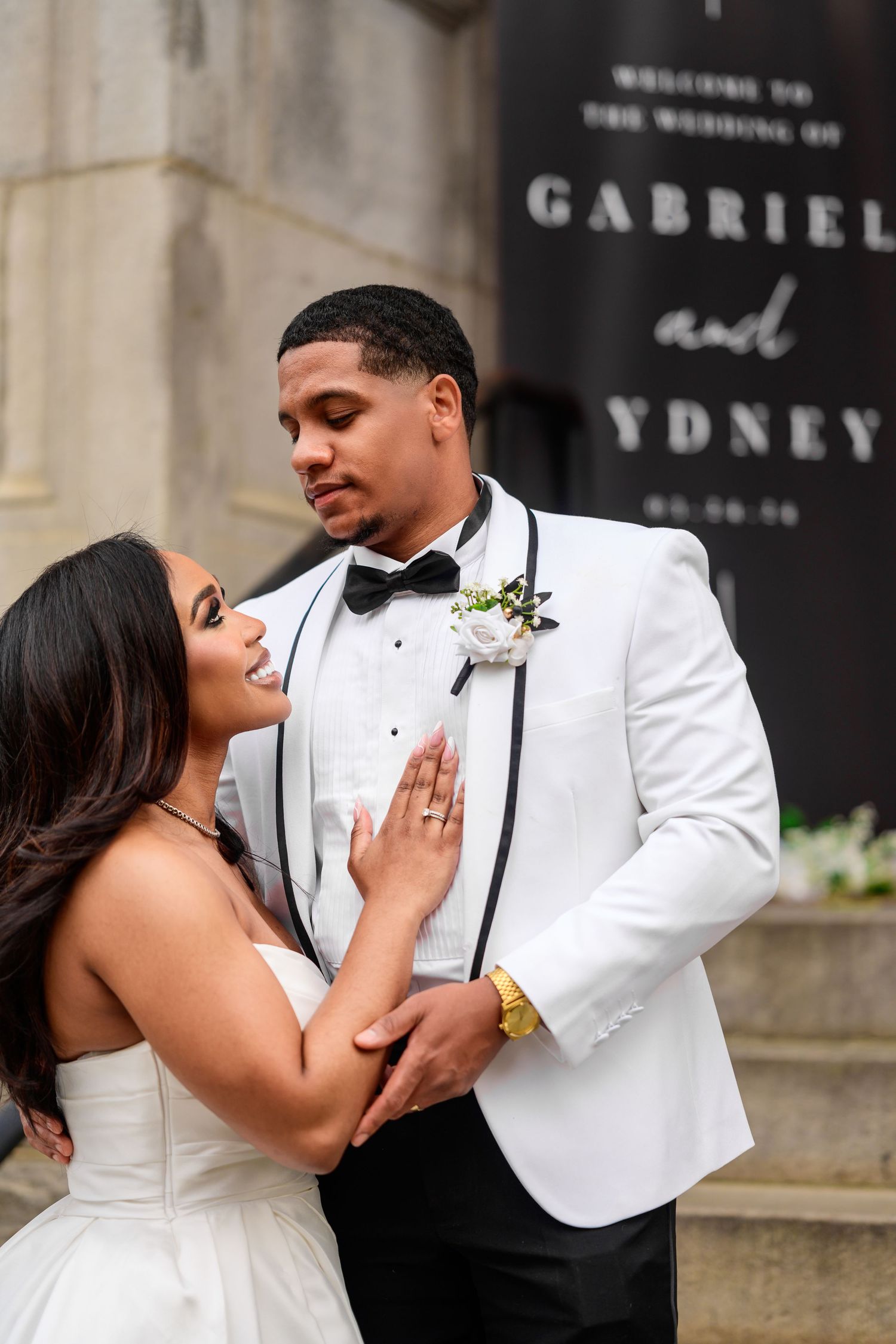Romantic wedding couple shares playful moments in formal attire near stone architecture.