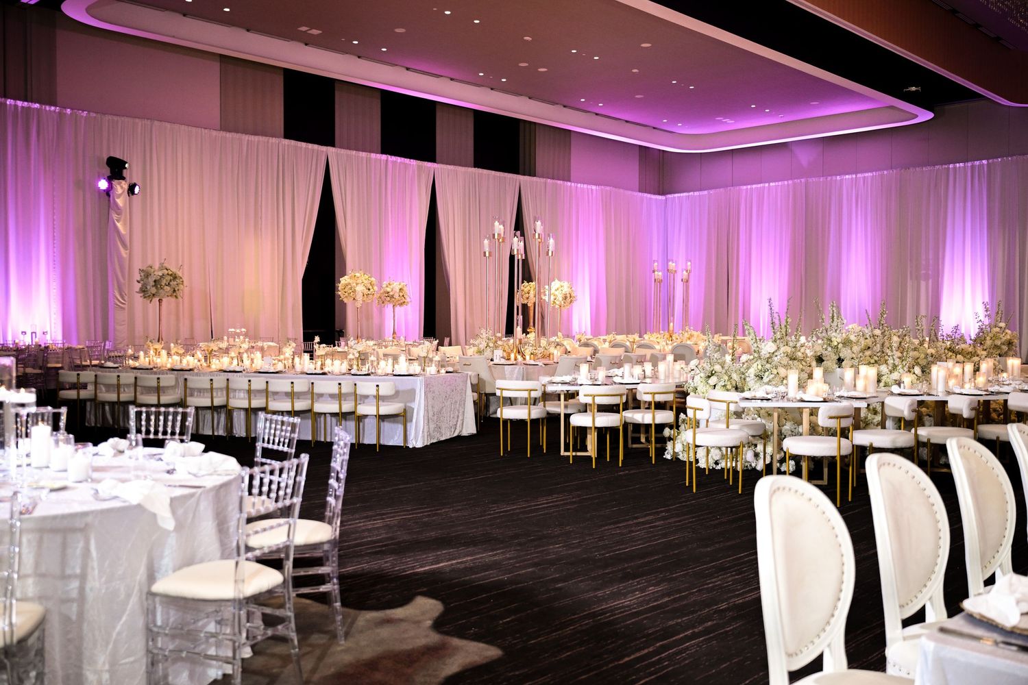 Modern ballroom wedding setup with white draping, dark flooring, and dramatic purple accent lighting.