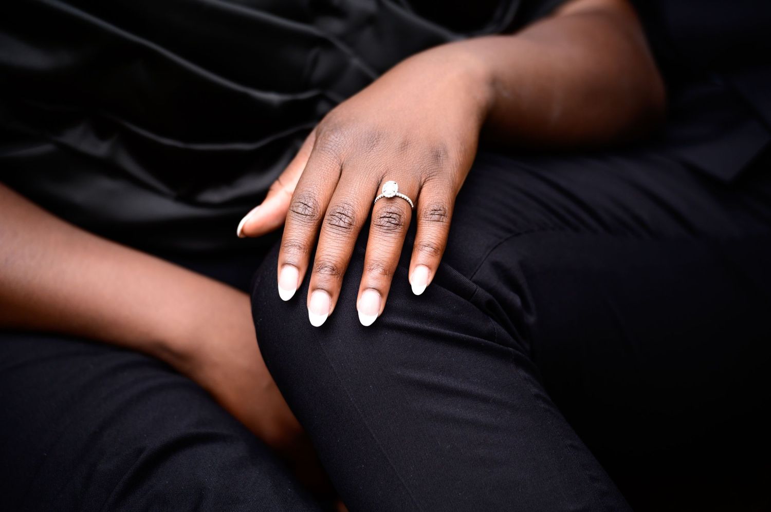 Close-up of manicured hand with engagement ring resting on black fabric.