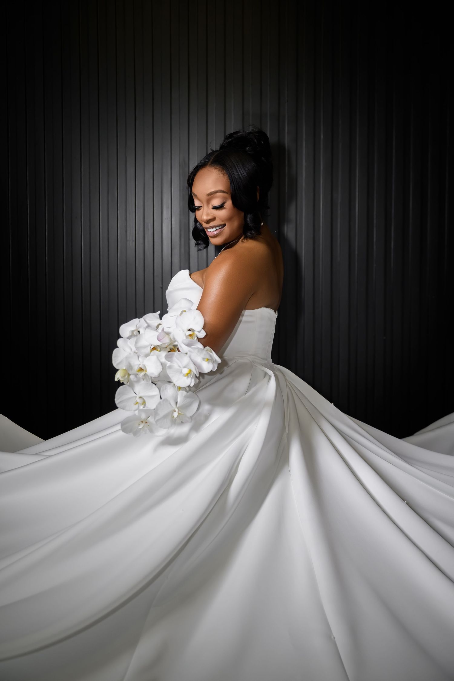 A stunning bridal portrait series showing a flowing white wedding gown with orchid bouquet against a dark backdrop.