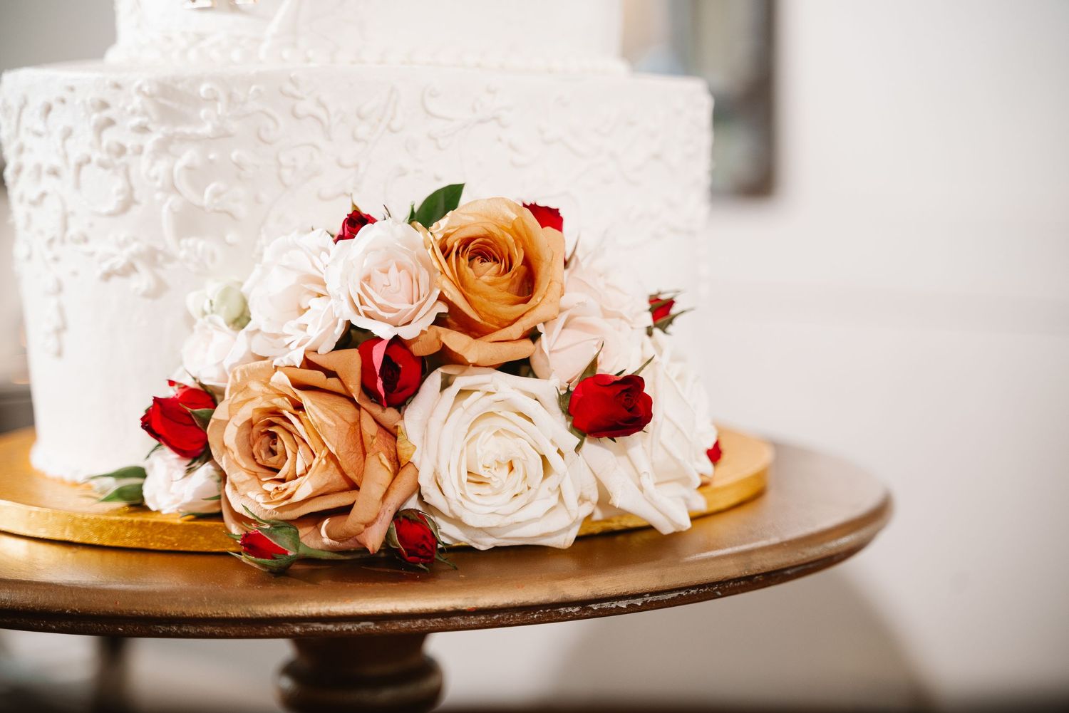 Close-up of wedding cake floral decorations featuring peach and burgundy roses with white frosting.