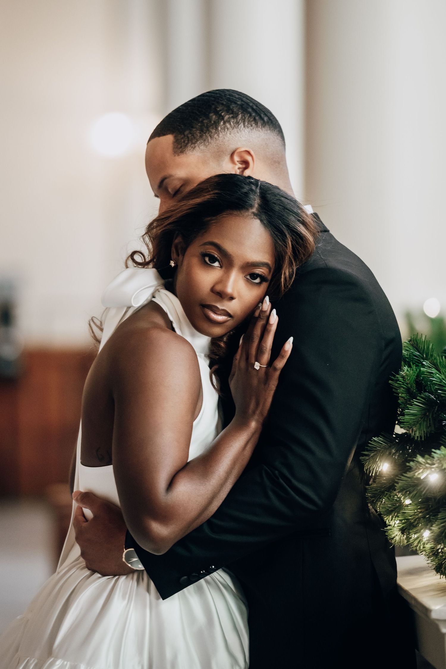 Intimate couple embracing in formal attire against white columns and holiday decor.