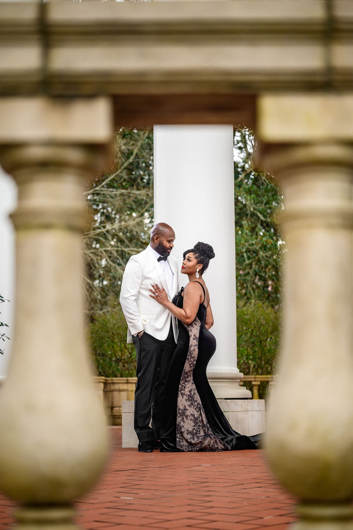 Romantic couple shares intimate moments during engagement photo session at elegant outdoor venue with white columns.