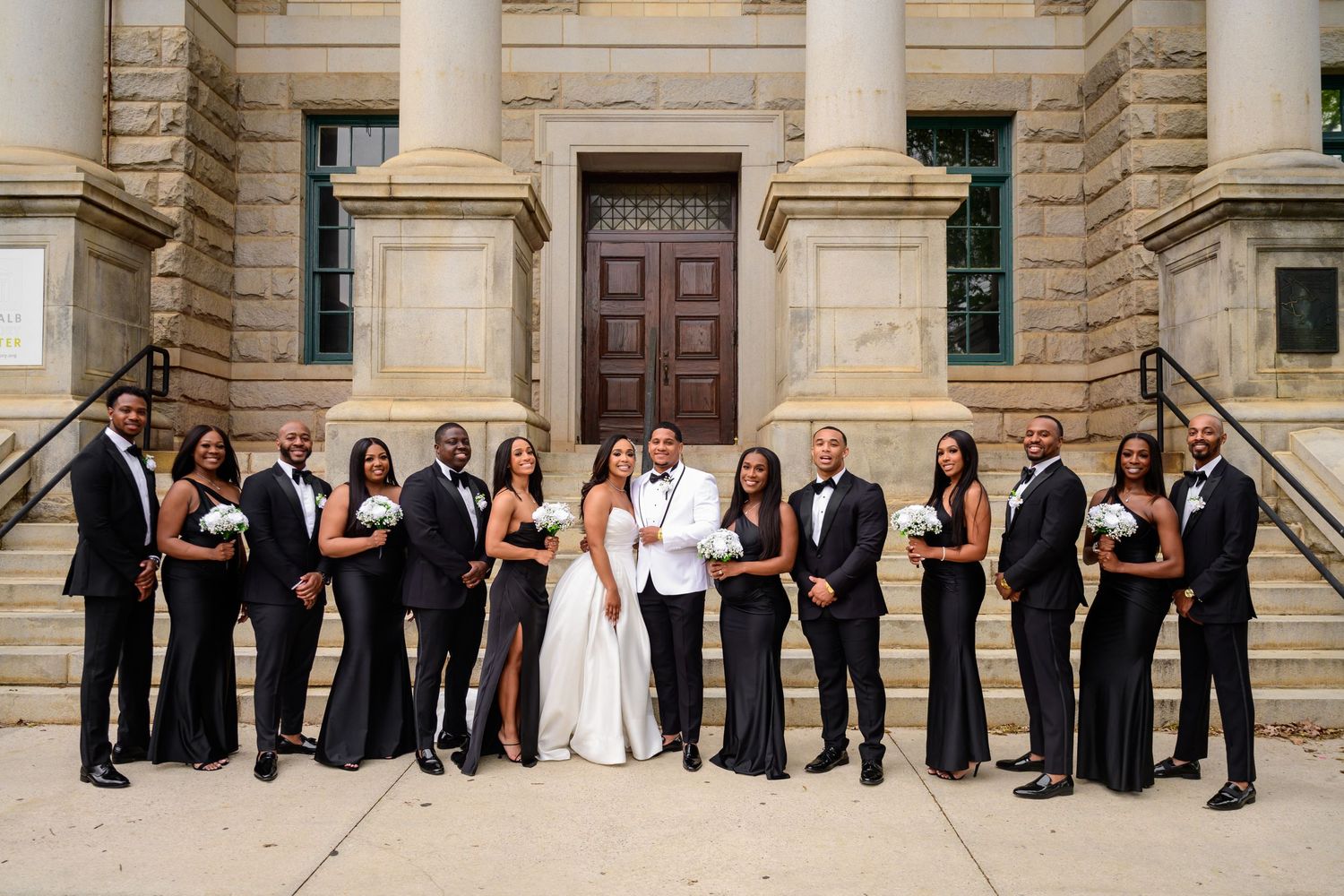 Elegant wedding party poses in front of grand stone building with columns.