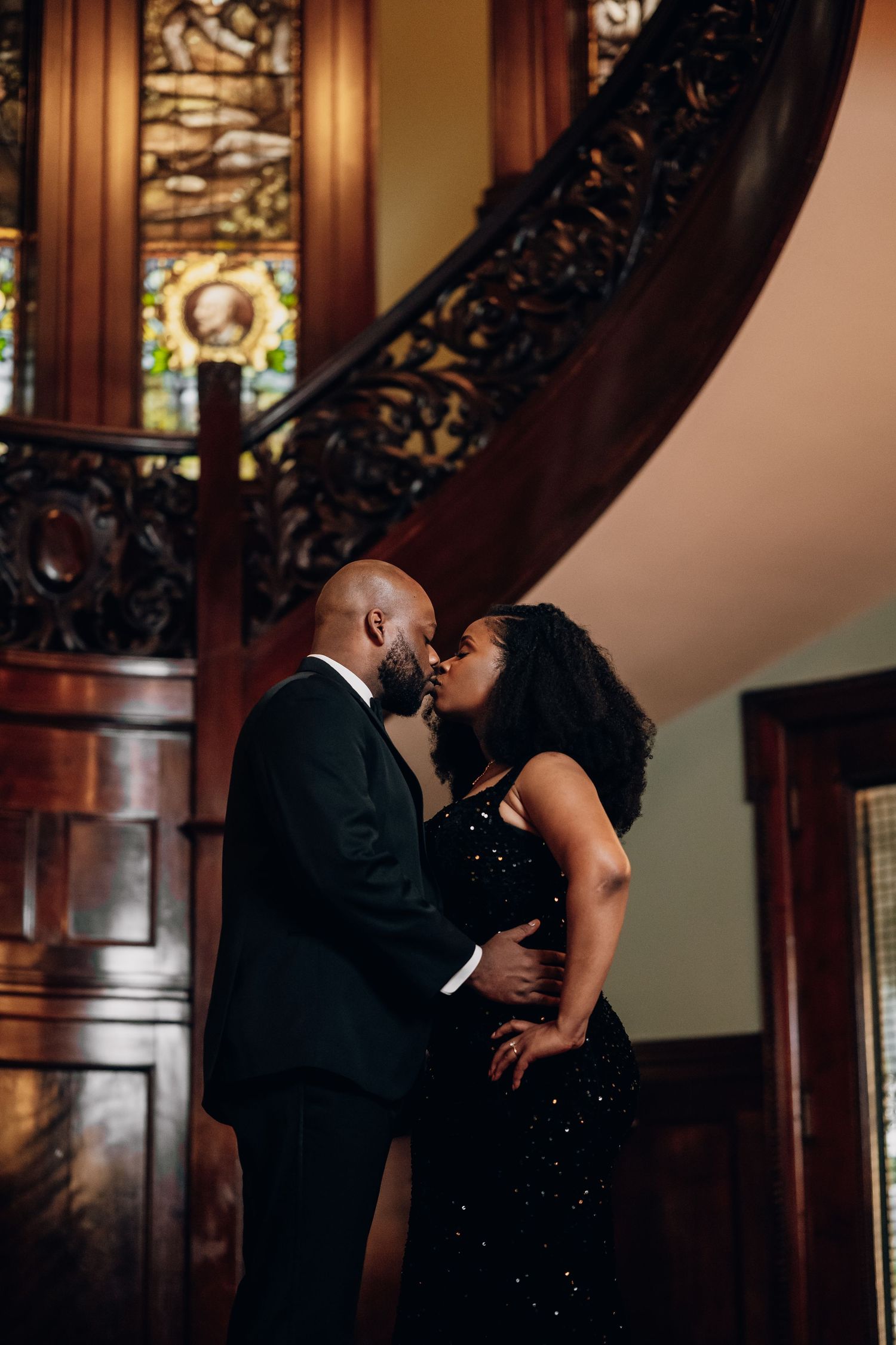 Romantic couple shares intimate moment on ornate staircase in formal evening wear.
