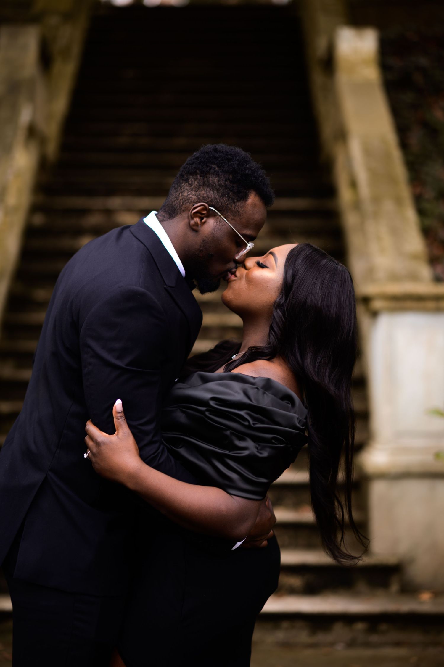 Romantic couple in formal wear share intimate moment on stone staircase.