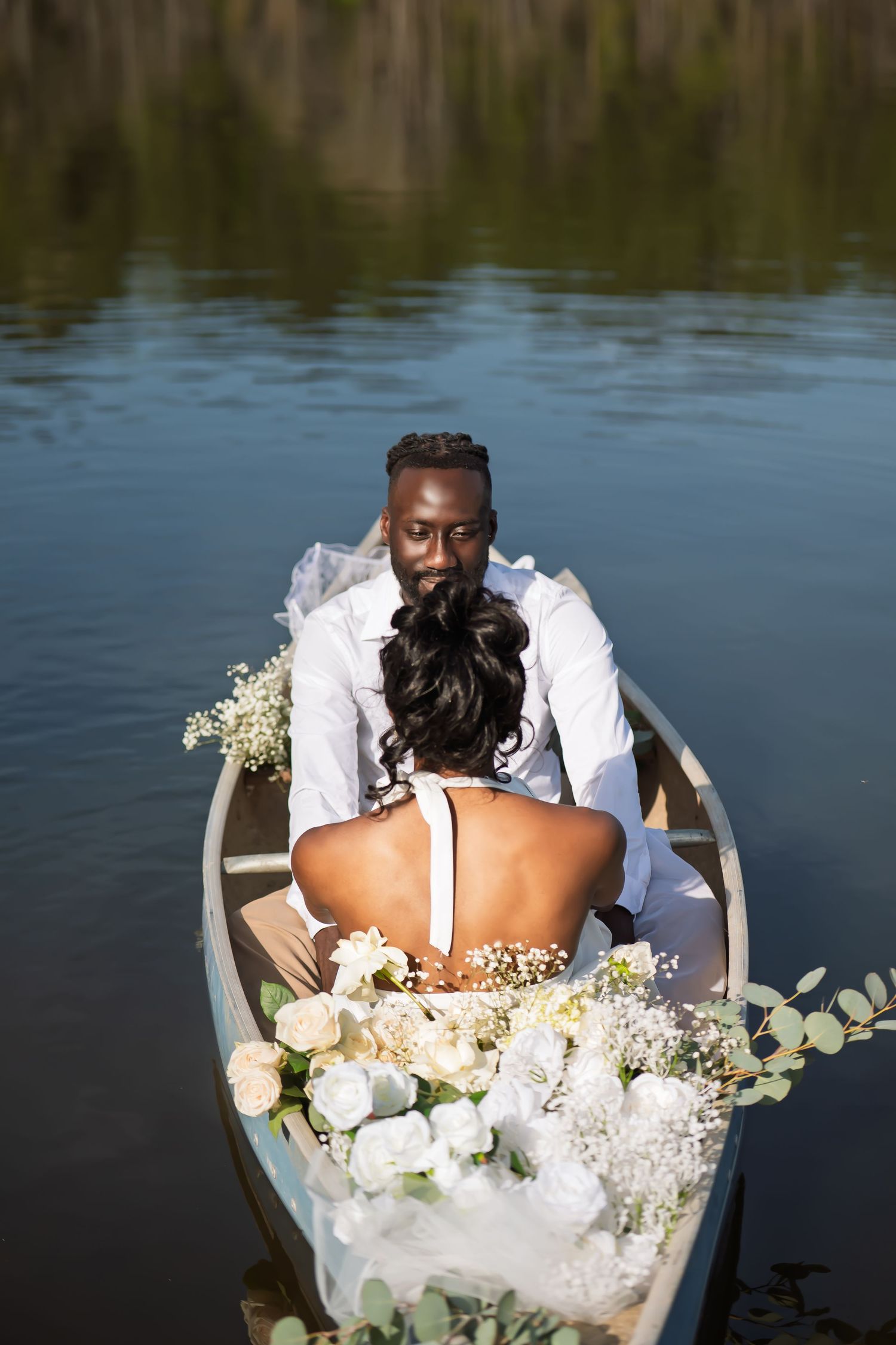 Intimate wedding photo of couple in white attire with floral decorations in canoe on lake.