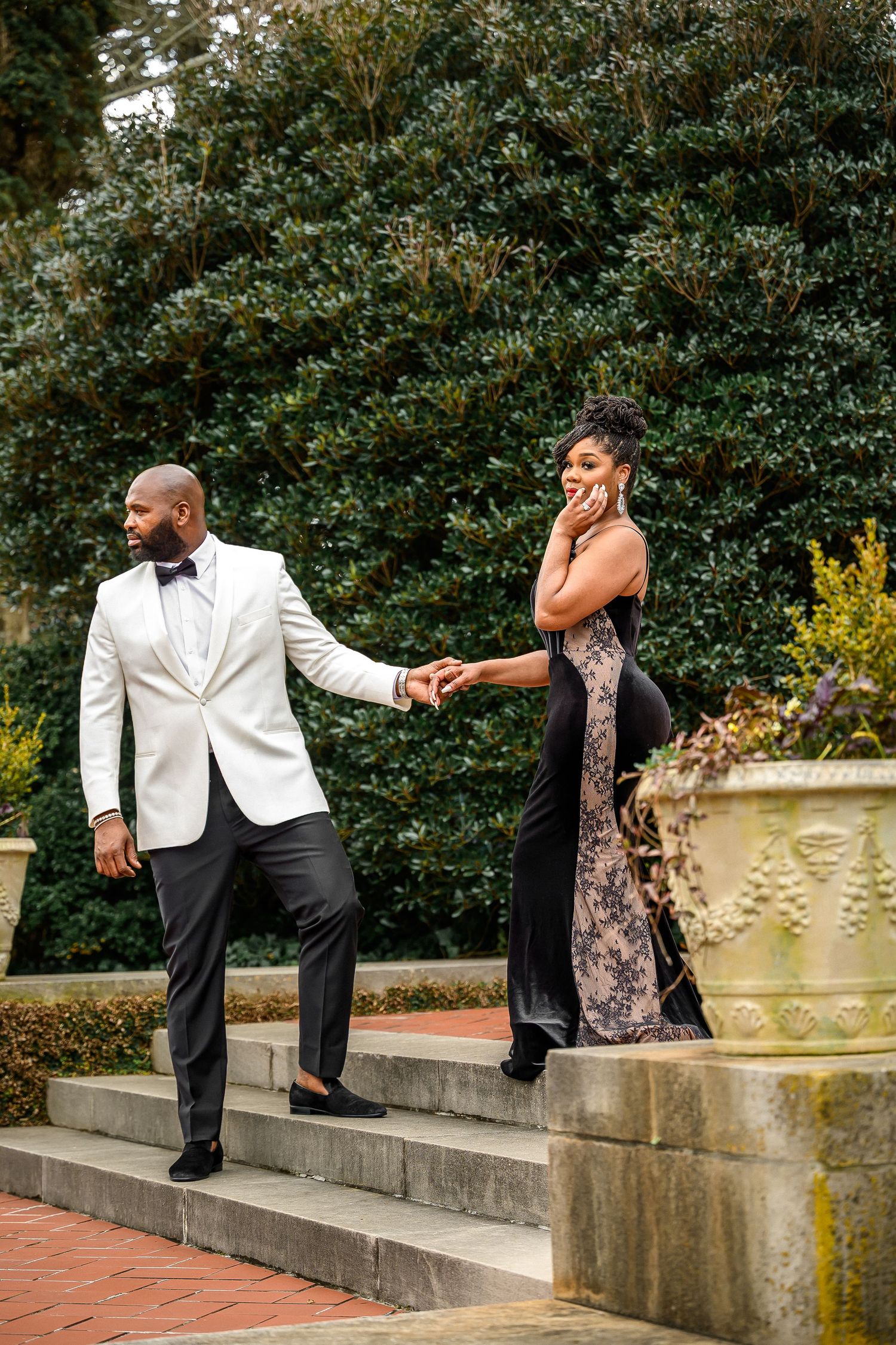 Couple dancing together on garden steps in formal attire with decorative planters and greenery in background.