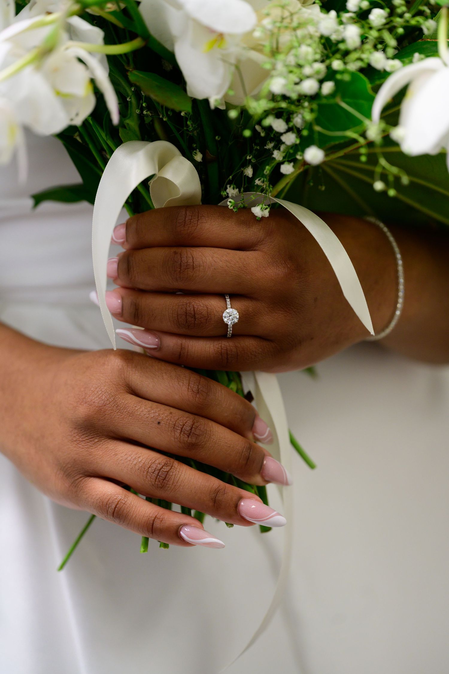 Elegant bridal hands holding white floral bouquet with engagement ring detail.