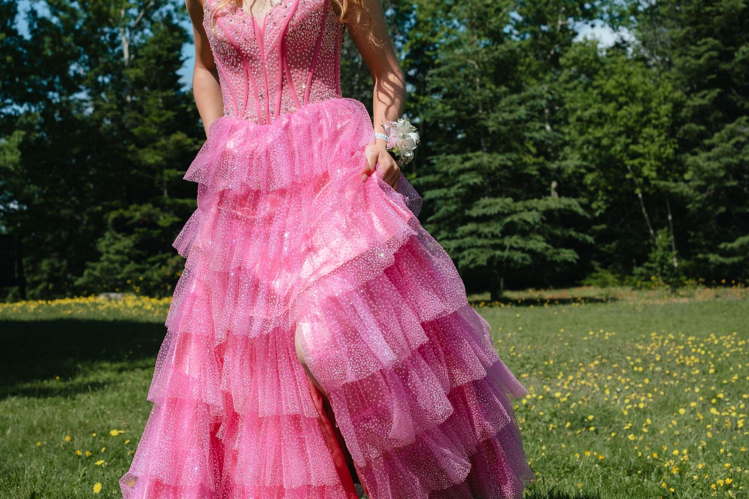 A pink tulle dress with ruffled layers flows gracefully in a sunny meadow filled with yellow wildflowers.