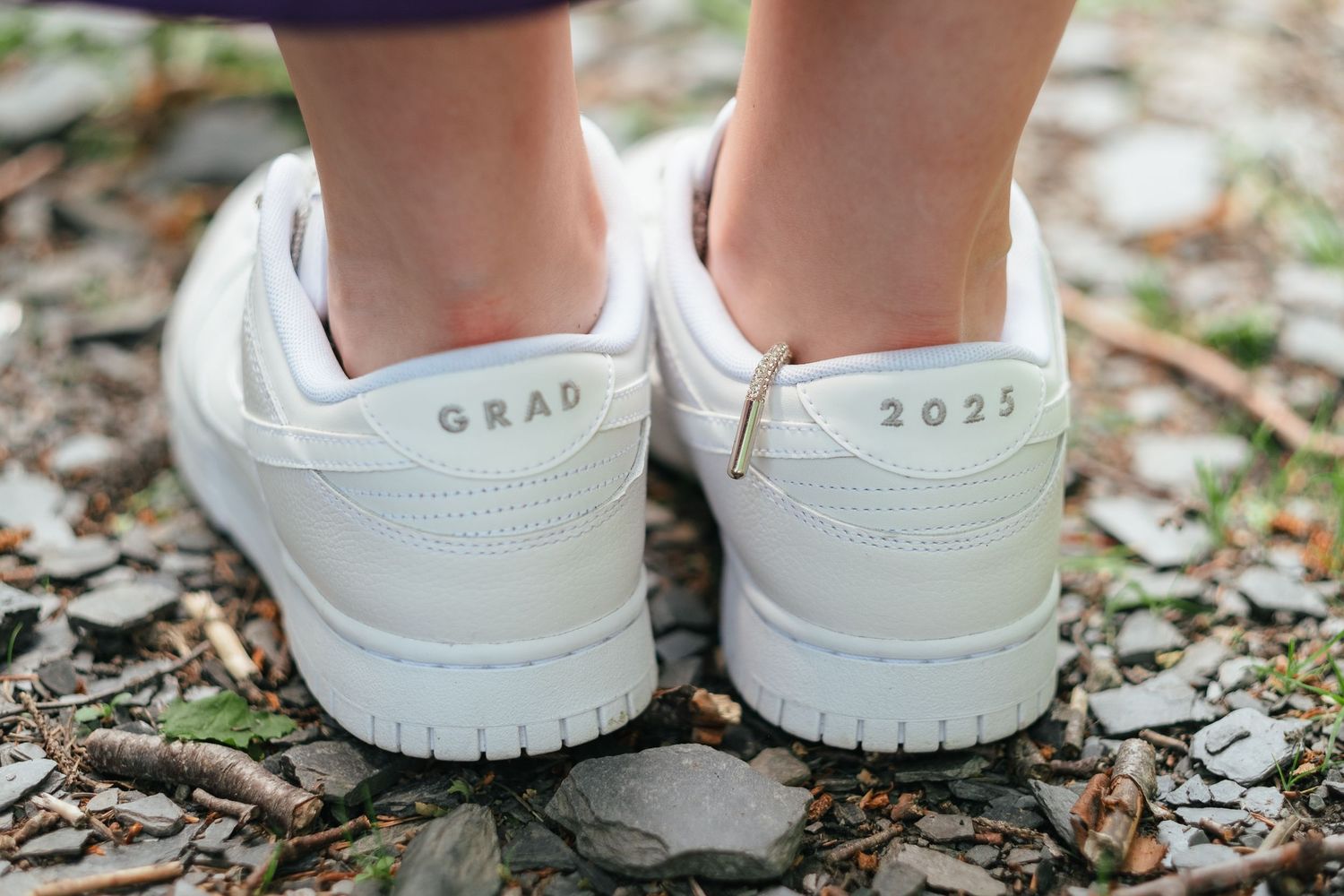 Close-up shots of white graduation sneakers with 'GRAD 2023' text on the heels resting on fallen leaves.