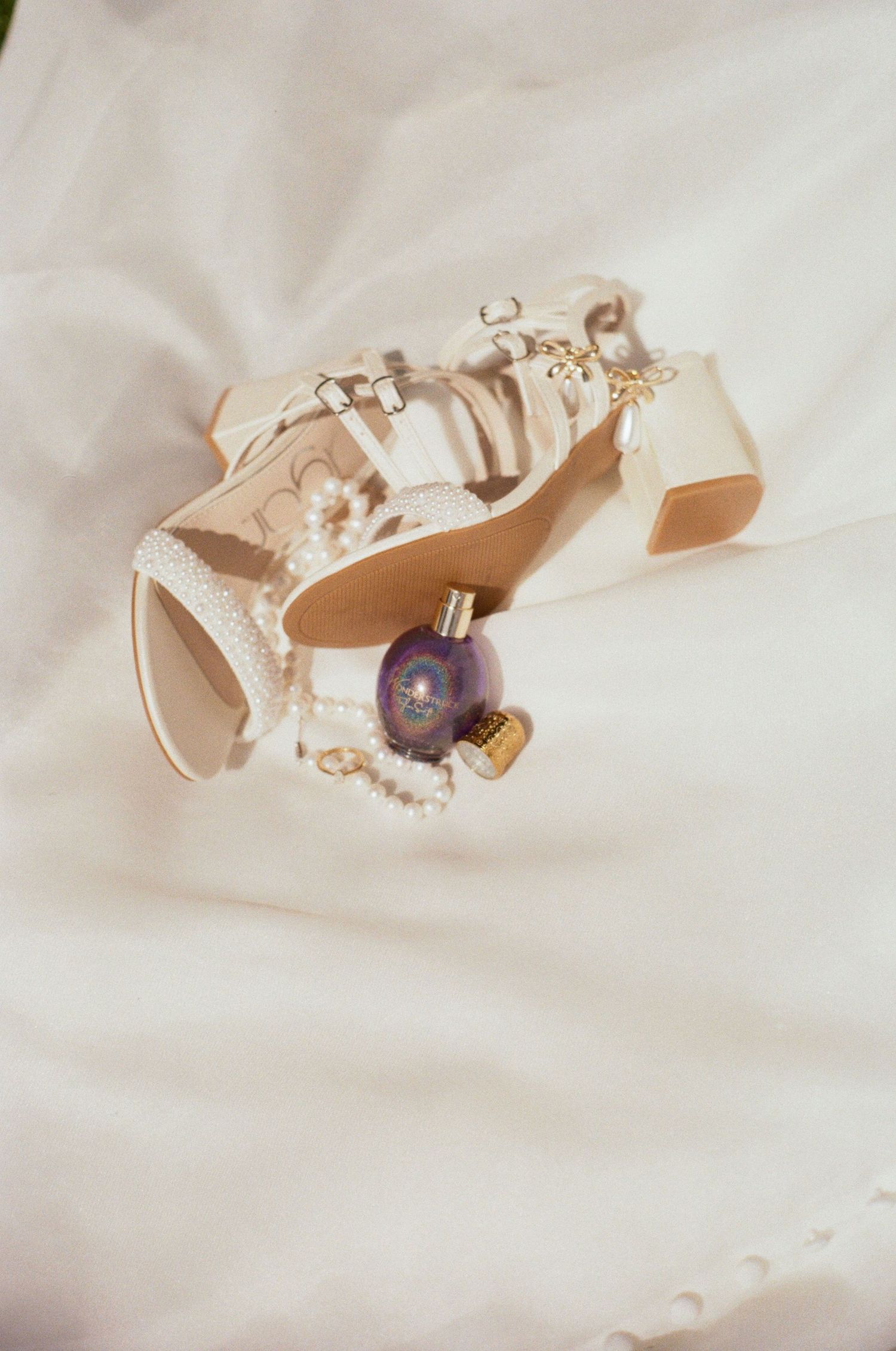 Elegant ivory wedding shoes with delicate lace details and pearl accents lay on white fabric.