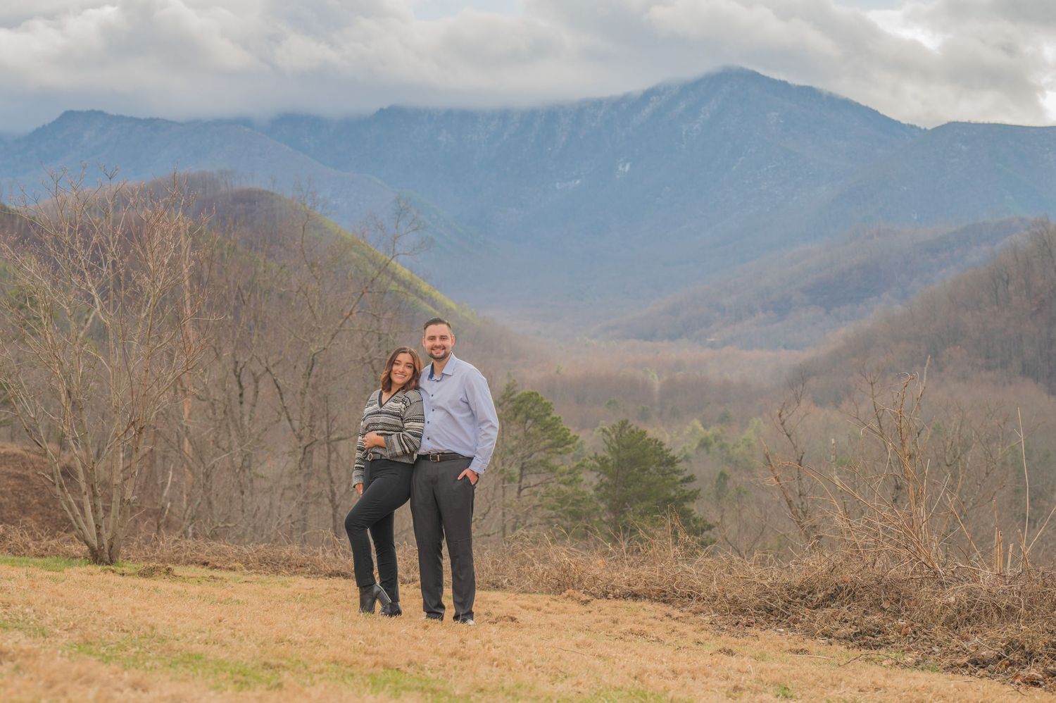 A couple stands together on a hilltop overlooking scenic mountain views in the Great Smoky Mountains by Pigeon Forge Photographer tn.