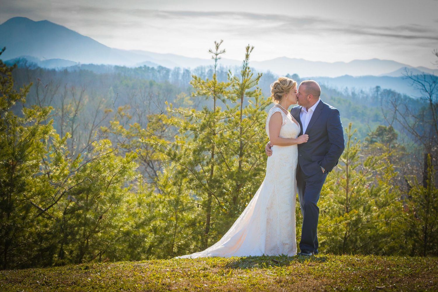 A wedding couple shares a romantic moment on a mountaintop surrounded by yellow spring foliage and a misty mountain backdrop.
