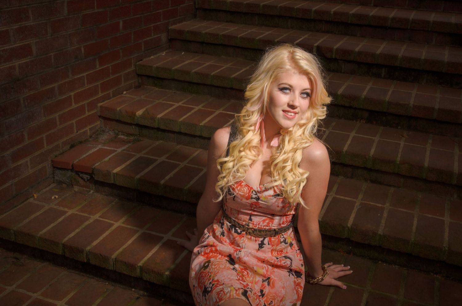 Person wearing a floral dress sits on brick stairs in warm lighting.