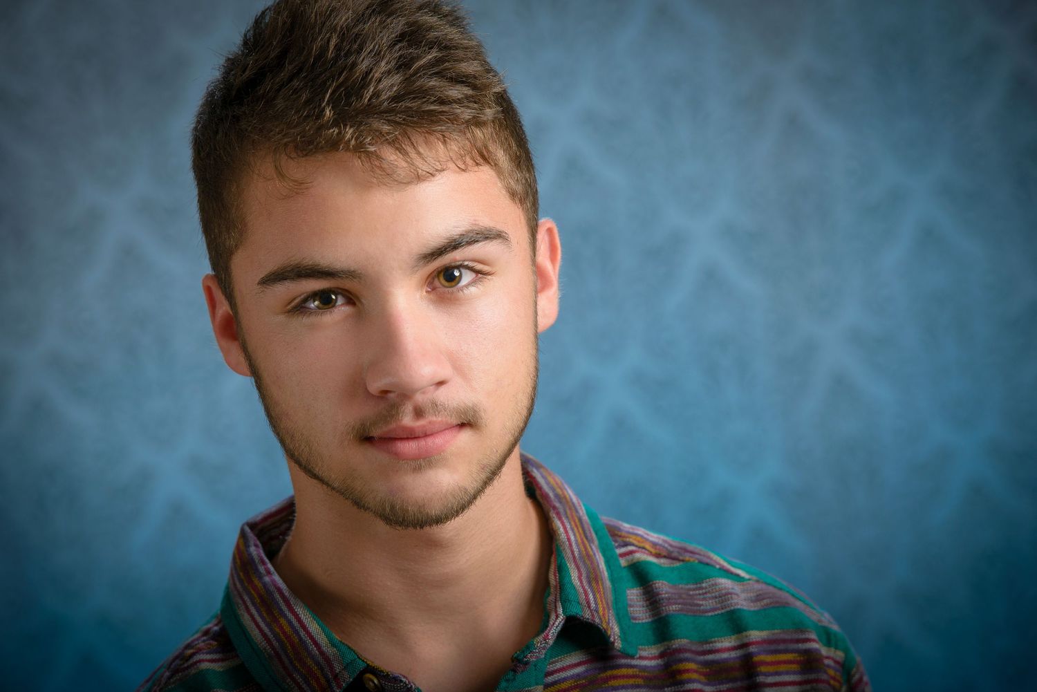 Portrait of young person wearing plaid shirt against blue studio backdrop.