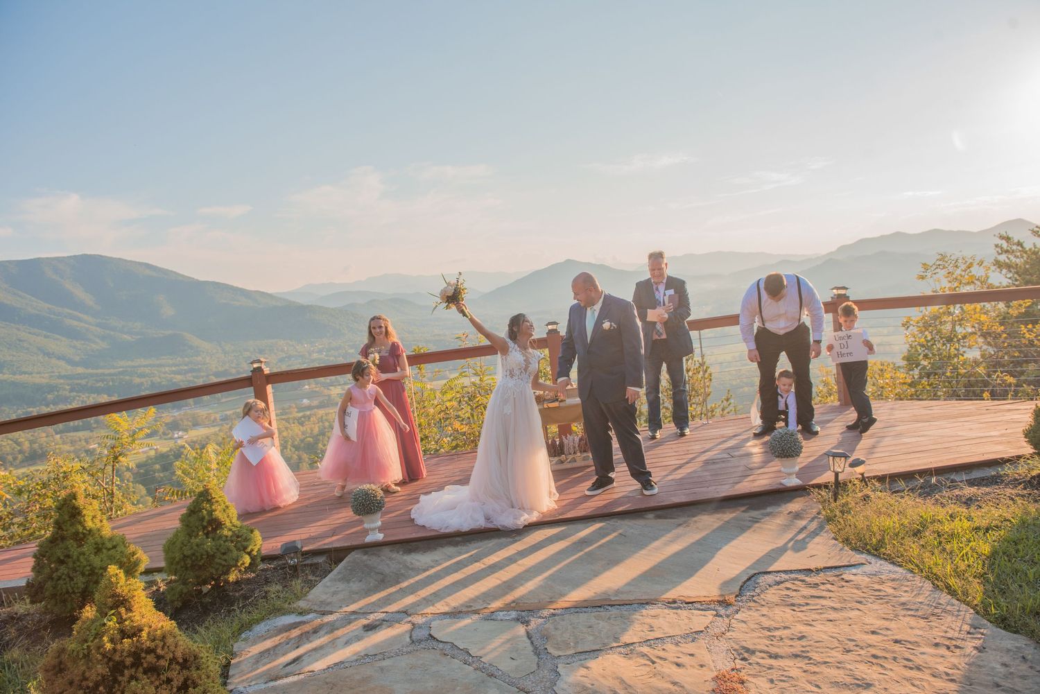 Wedding party celebrates on a scenic mountain overlook with beautiful rolling hills in the background during sunset.