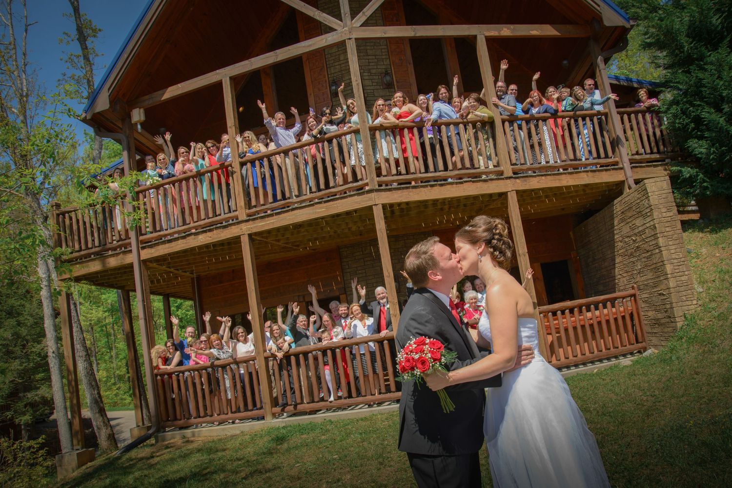 A couple shares a romantic moment at their mountain lodge wedding while guests cheer from the balcony above by Pigeon Forge Photographers.