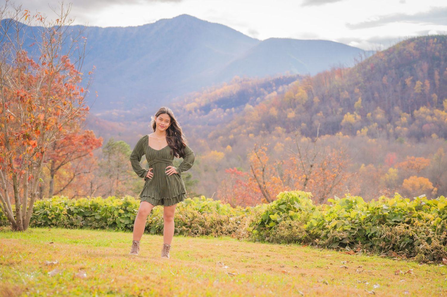 A person poses in a green dress against a backdrop of mountains and vibrant fall foliage in the Smoky Mountains.