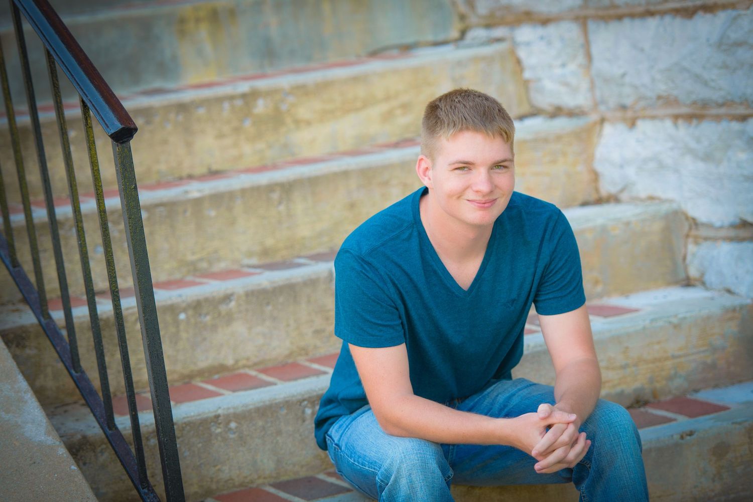 Someone in a teal v-neck shirt sits casually on stone steps against a textured wall backdrop.