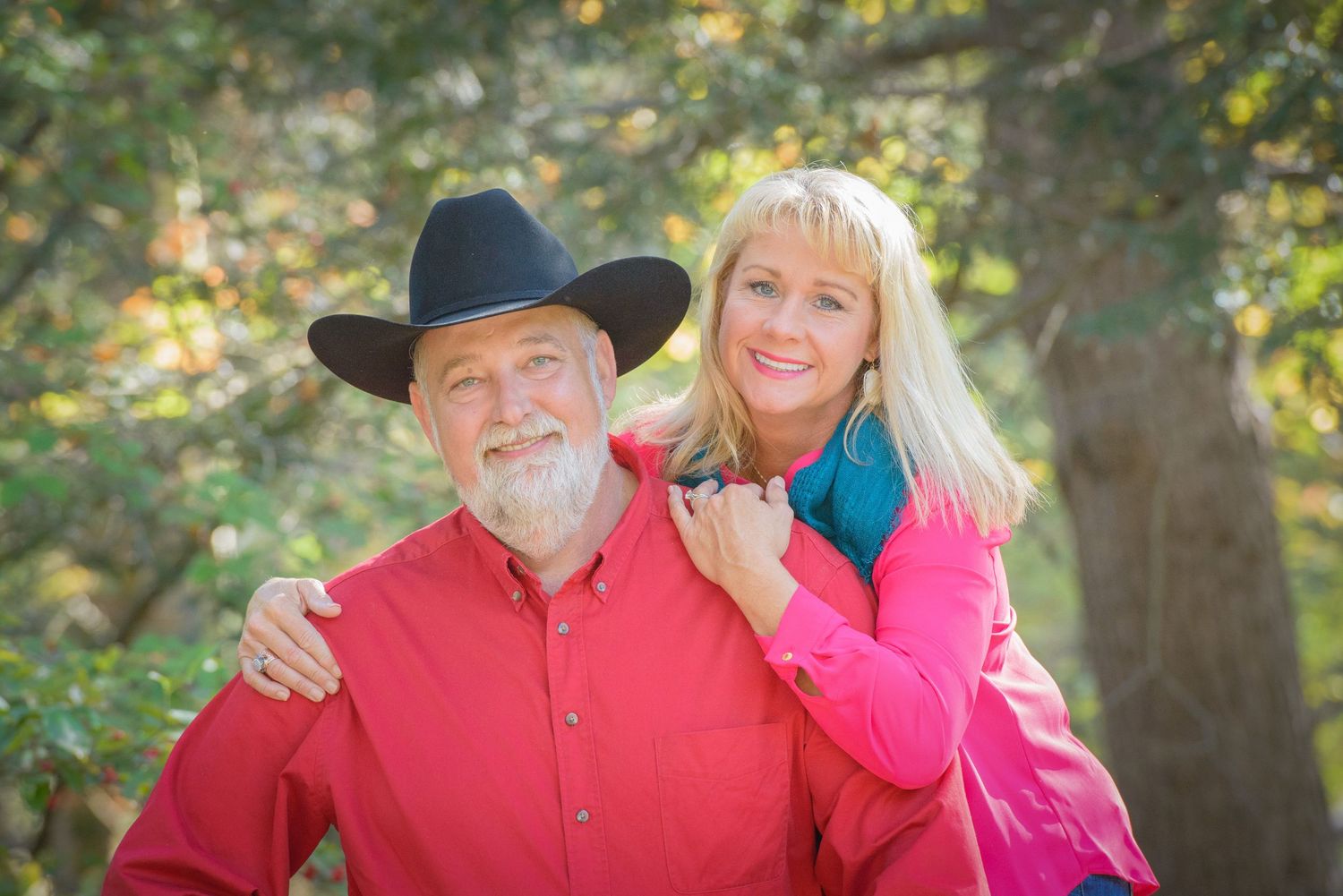 A person in a red button-down shirt and black cowboy hat poses with wife wearing bright pink outdoors in nature by Sevierville Photographers