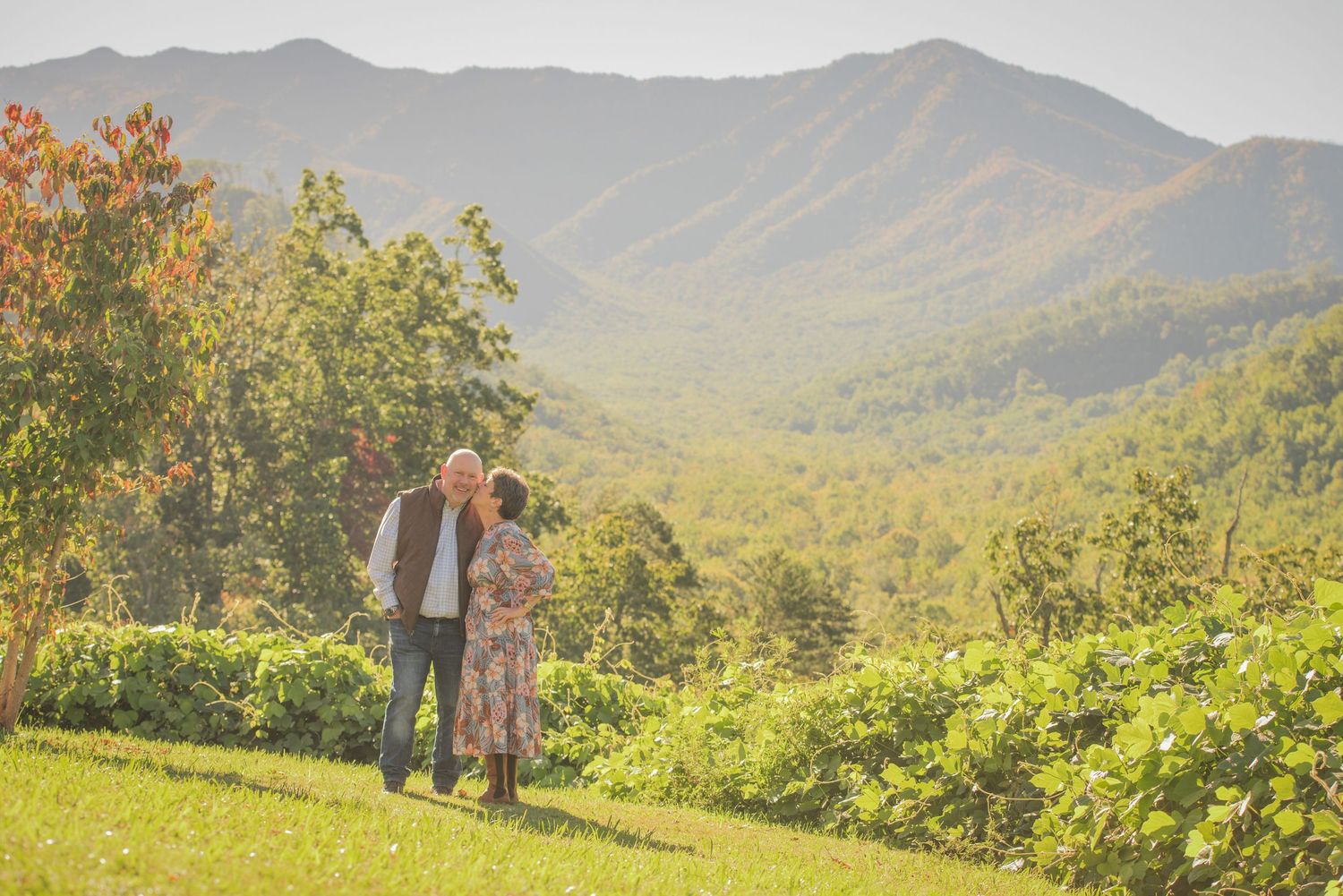 Two figures stand together on a grassy hillside overlooking a scenic mountain valley with lush green forest views by Gatlinburg Photographer