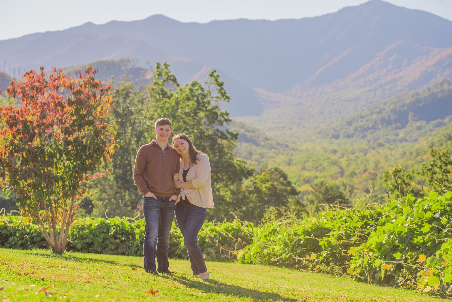 A couple enjoys a scenic mountain view together on a grassy hillside with fall foliage and rolling hills by Gatlinburg TN Photographers.