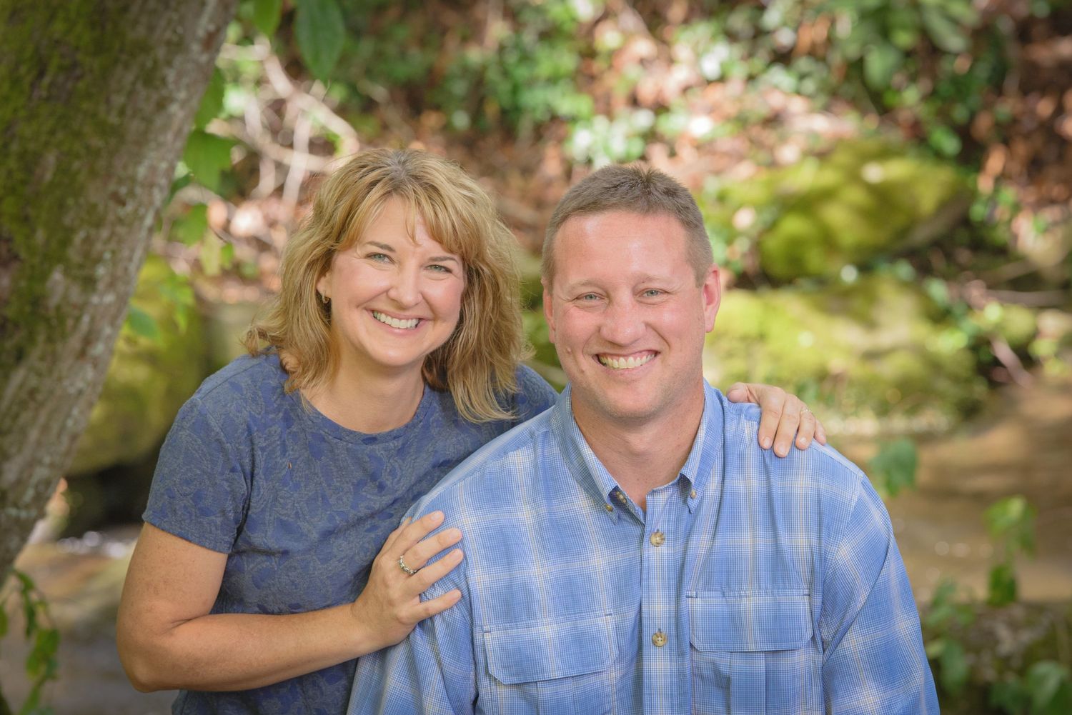 A couple pose together outdoors in casual attire with a blurred garden background in warm natural lighting by Sevierville TN Photographers.