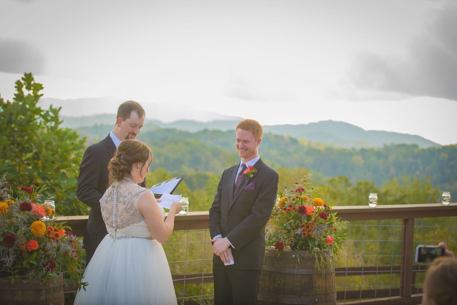 A mountain wedding ceremony taking place on a rustic deck adorned with orange flowers and scenic mountain views in wears valley TN.