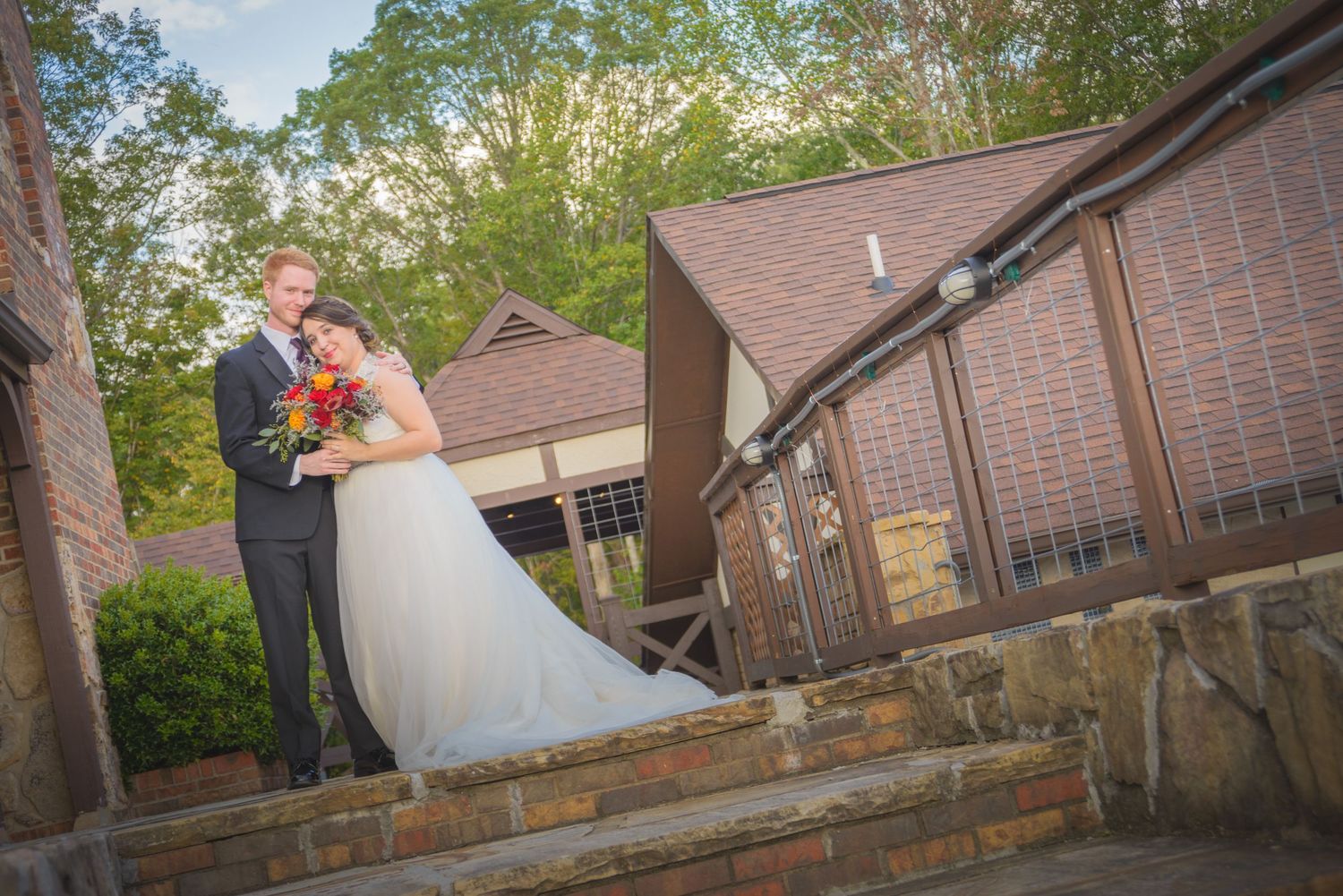 A couple shares a romantic moment on rustic stone steps outside a brown brick building surrounded by greenery in Pigeon Forge TN.