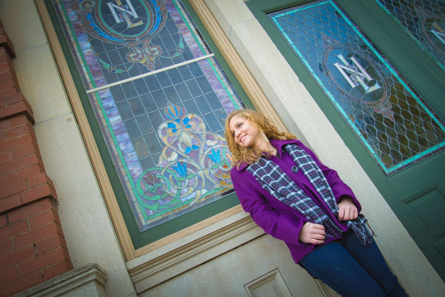 Someone in a purple sweater sits casually against a wall with decorative stained glass windows and brick detailing.