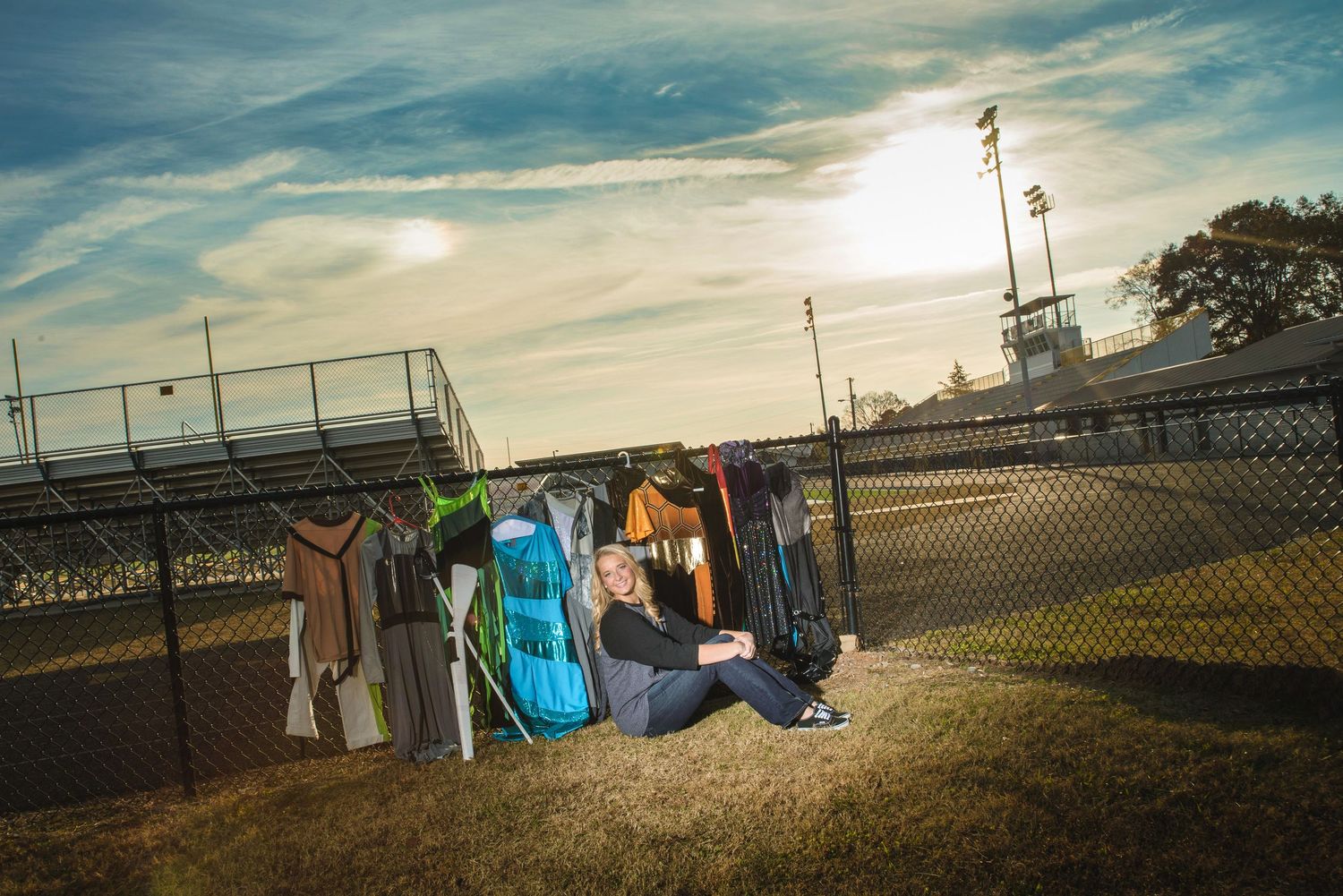 Baseball equipment and gear bags sit along a chain-link fence at sunset on a baseball field.