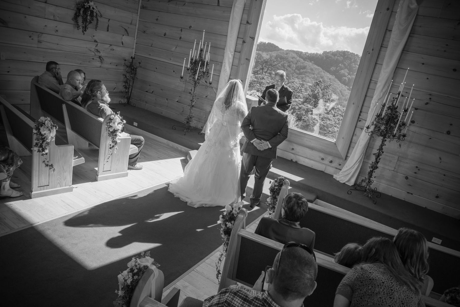 Black and white photograph of a wedding ceremony taking place in a rustic mountain venue with large windows by Pigeon Forge Photographers.