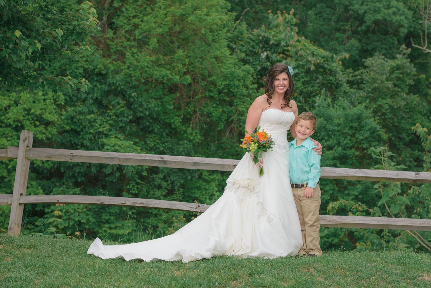 Pigeon Forge Wedding Photographers portrait of a bride in a flowing white lace gown stands with a young boy by a wooden fence.