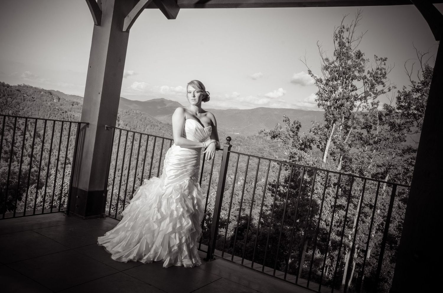 Sevierville wedding Photographer portrait of a bride in a flowing white gown poses on a mountain overlook porch with scenic hills.
