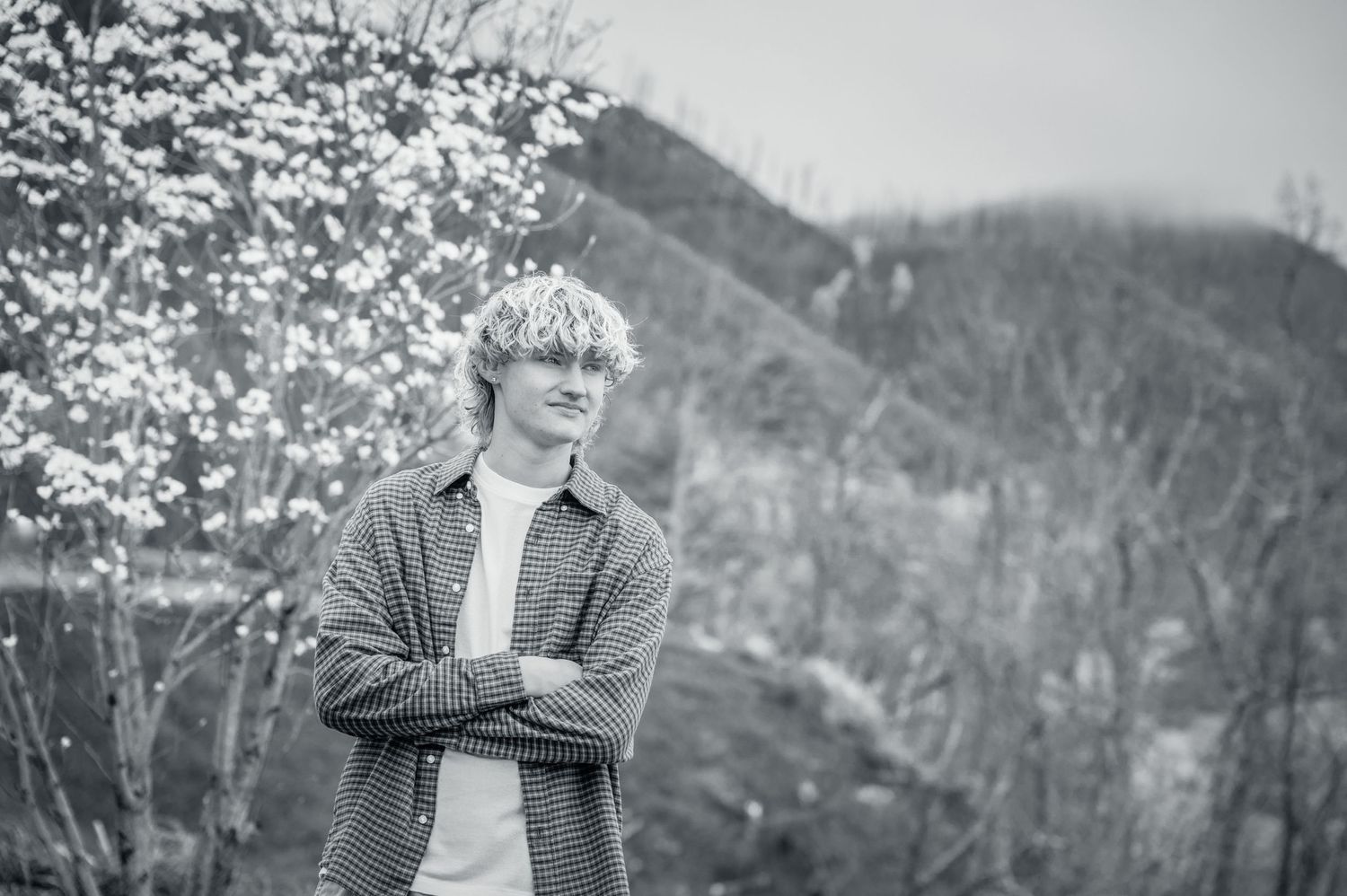 A black and white portrait of someone standing outdoors near blooming spring trees with Smoky Mountains in Background School Pictures