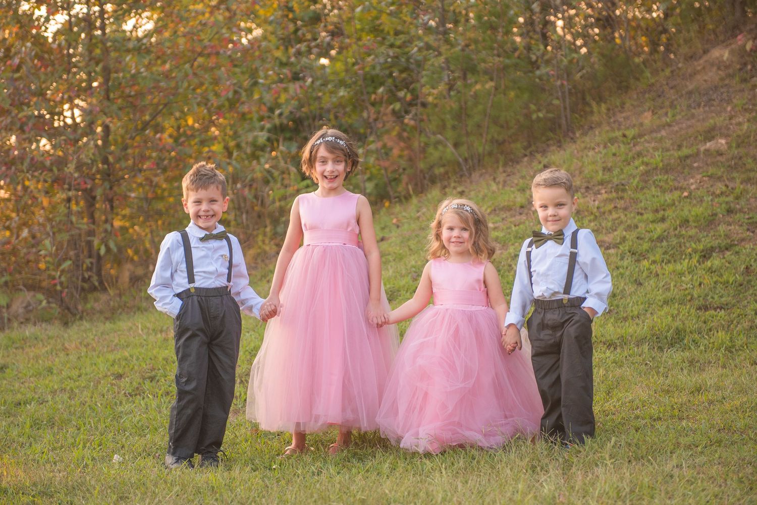 Two children in navy suspenders and two in pink tulle dresses stand together on a grassy hillside during autumn by gatlinburg photographers