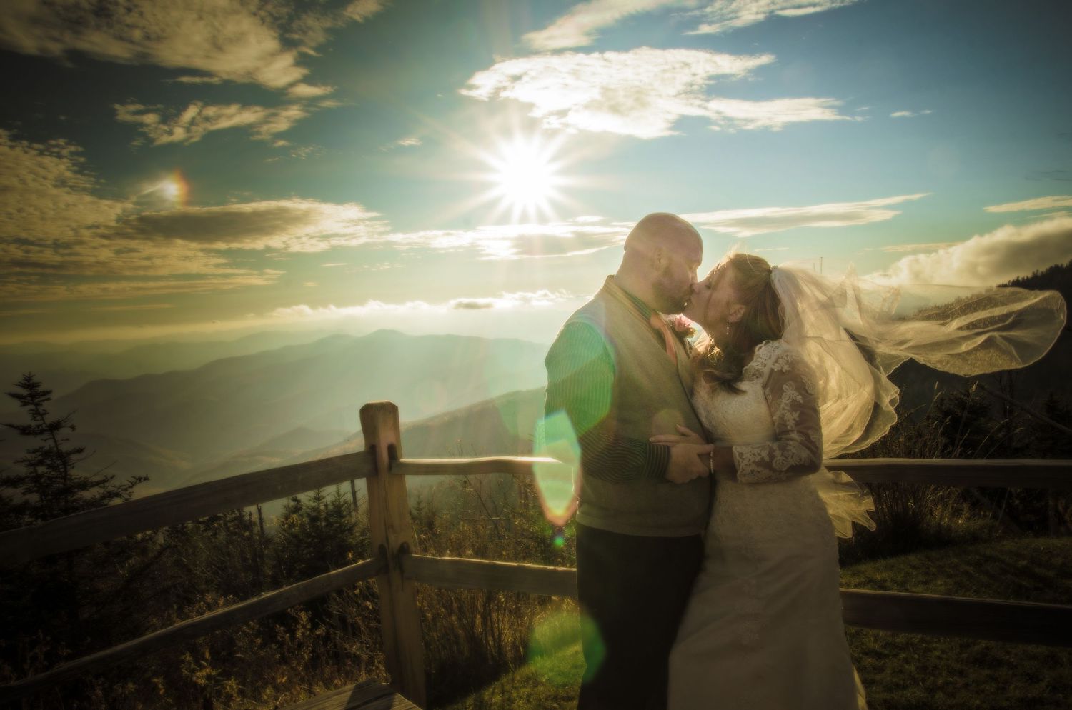 Romantic sunset silhouette on mountain overlook with dramatic lens flare and wooden railing against dramatic sky, the Great Smoky Mountains.