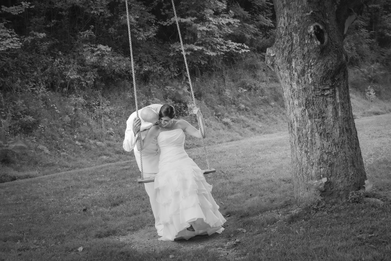 Black and white photo showing someone in a wedding dress swinging from a rustic rope swing near a tree by Pigeon Forge Photographers.