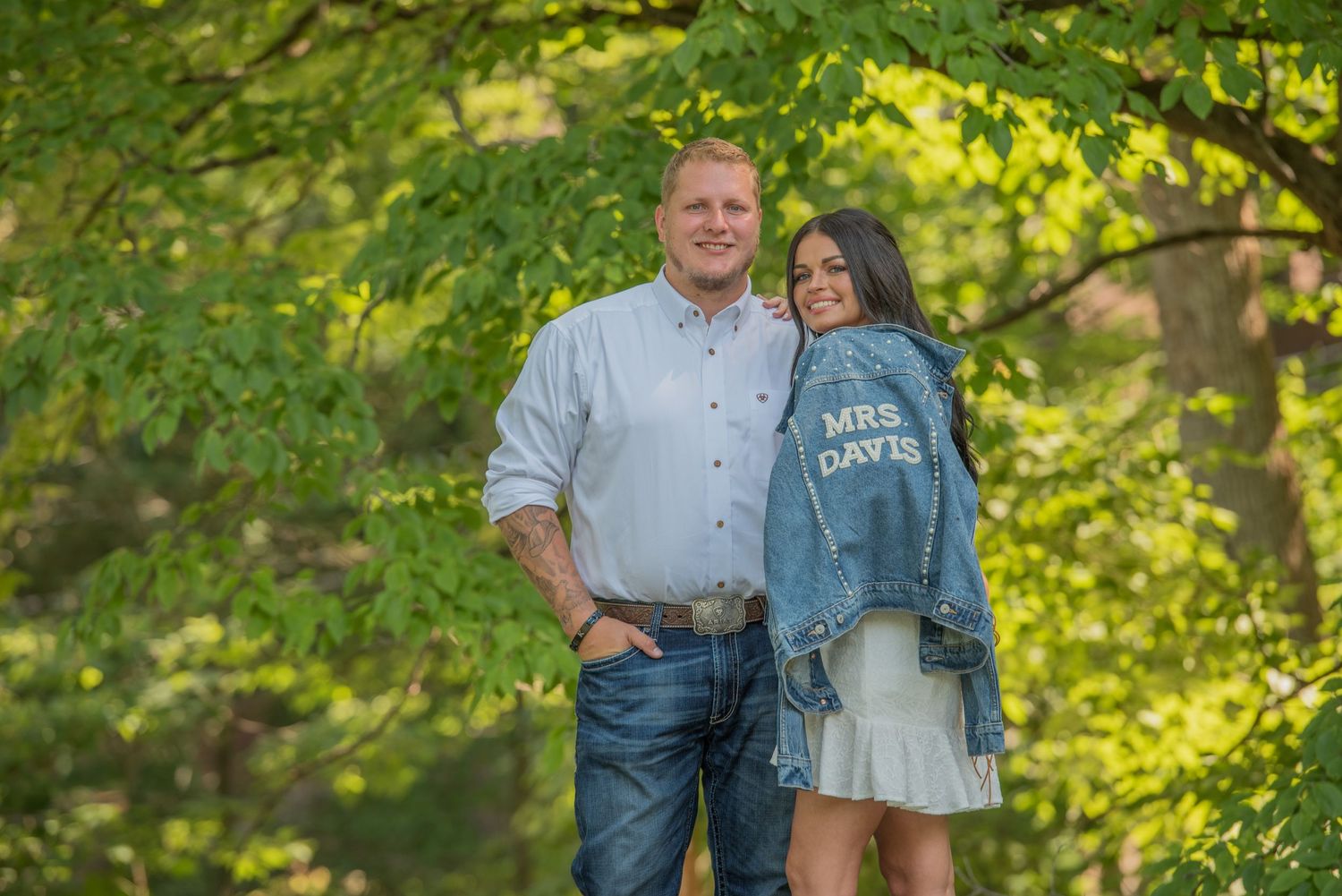 Engagement couple stand together outdoors in casual wear against a background of lush green trees by Engagement Photographer Gatlinburg.
