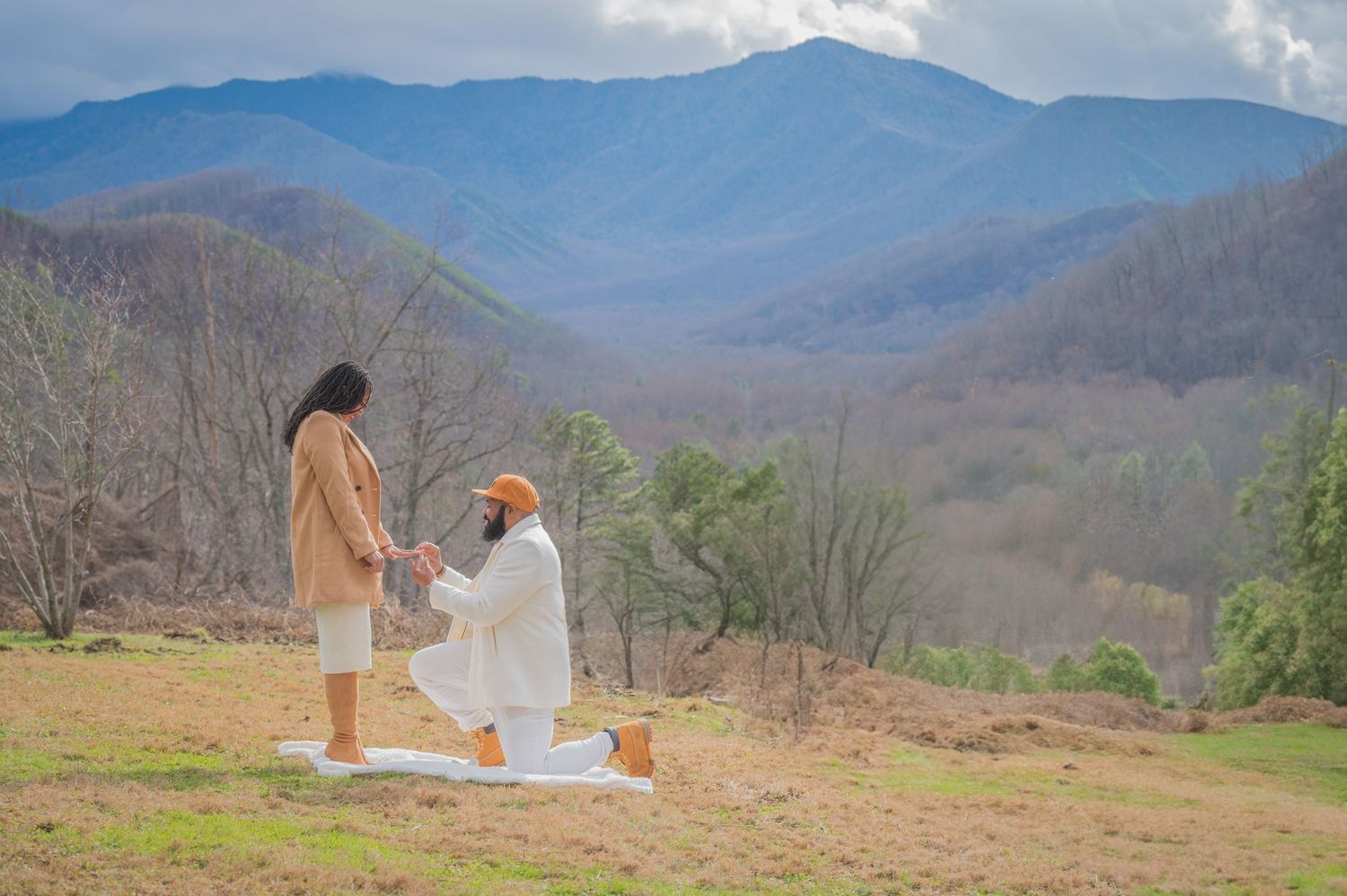 A romantic proposal moment on a scenic mountain overlook with rolling blue mountains and cloudy skies in the background in Gatlinburg.