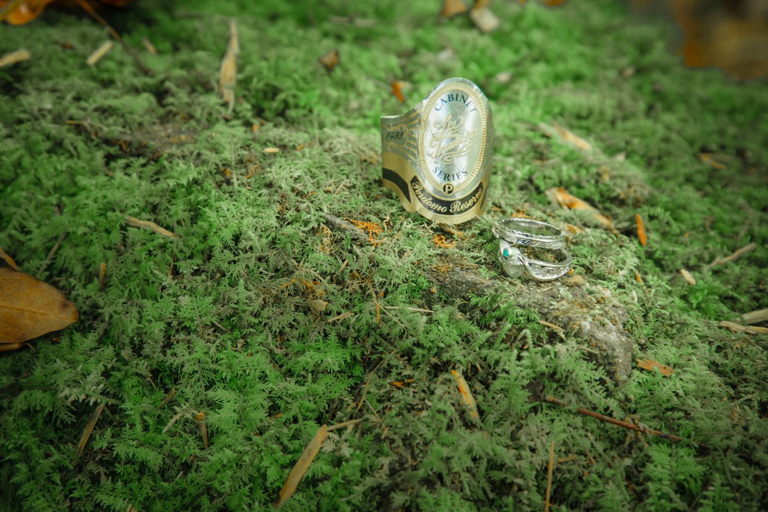 A small glass jar or vial sits on green moss-covered ground surrounded by scattered fallen leaves by Gatlinburg Wedding Photographers.
