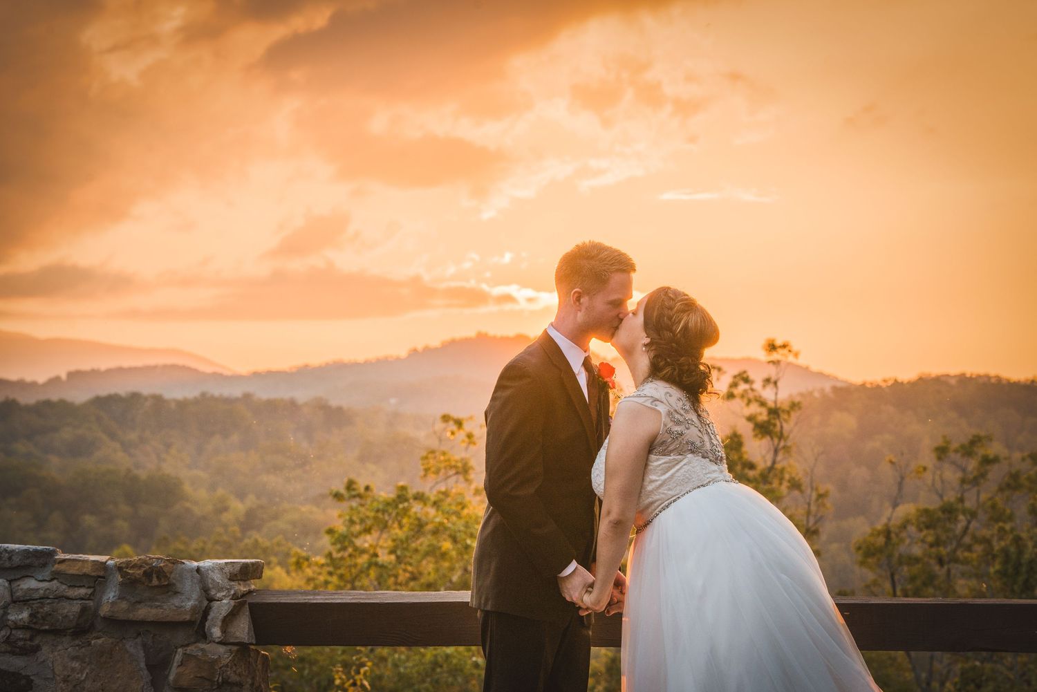 Gatlinburg TN Weddings couple in wedding attire share an intimate moment at sunset on a scenic mountain overlook with warm orange skies.