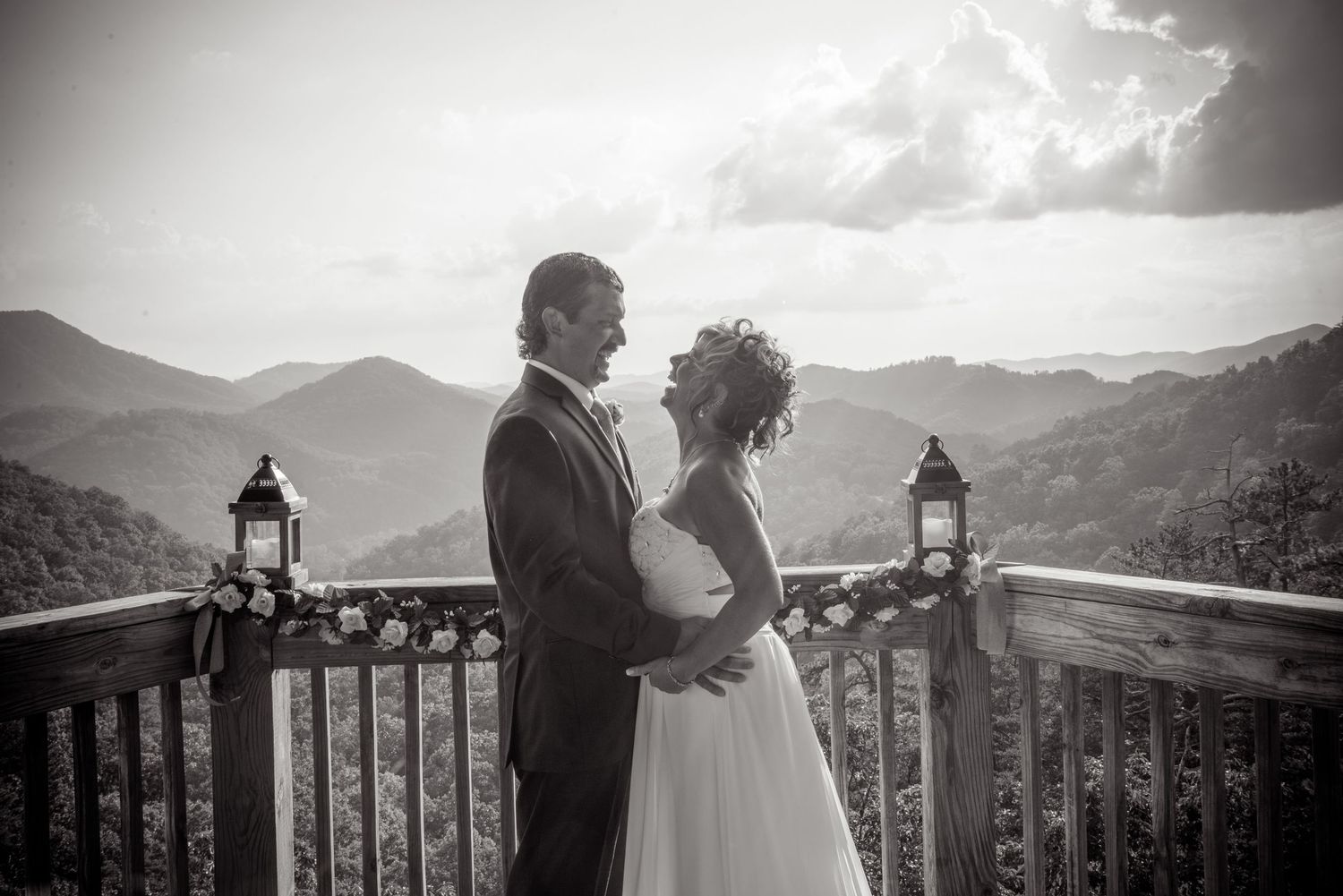 A couple shares a romantic moment on a mountain balcony with lanterns and scenic mountain views in black and white by Gatlinburg Weddings.