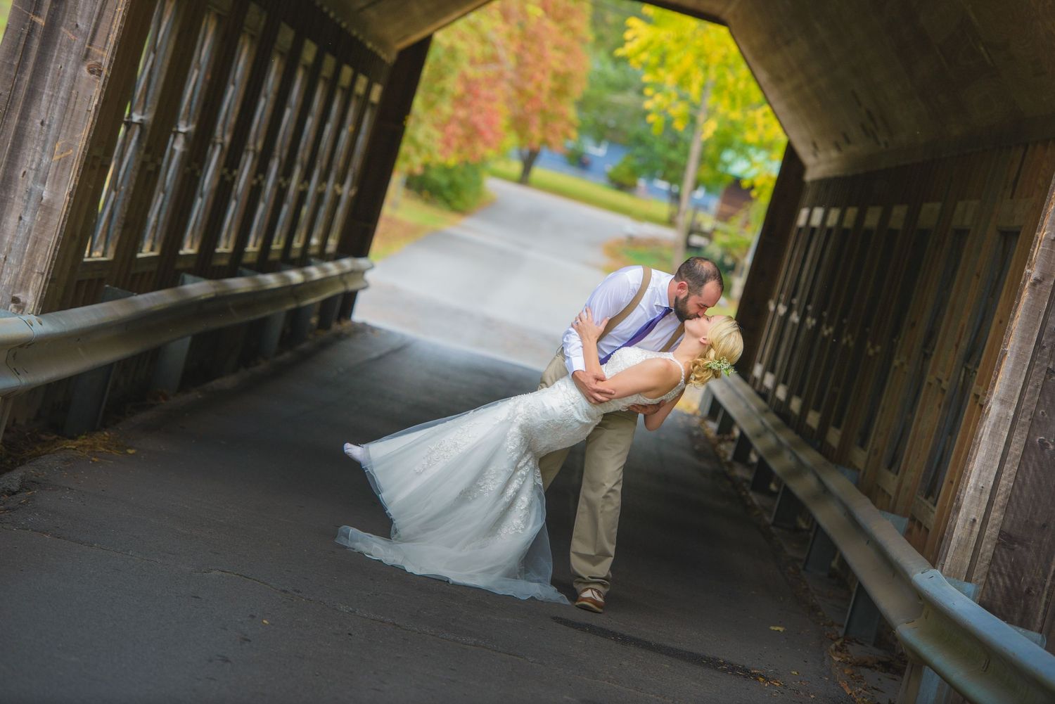A romantic dip pose captured under a covered wooden bridge during autumn with fall foliage in the background by Gatlinburg Weddings.