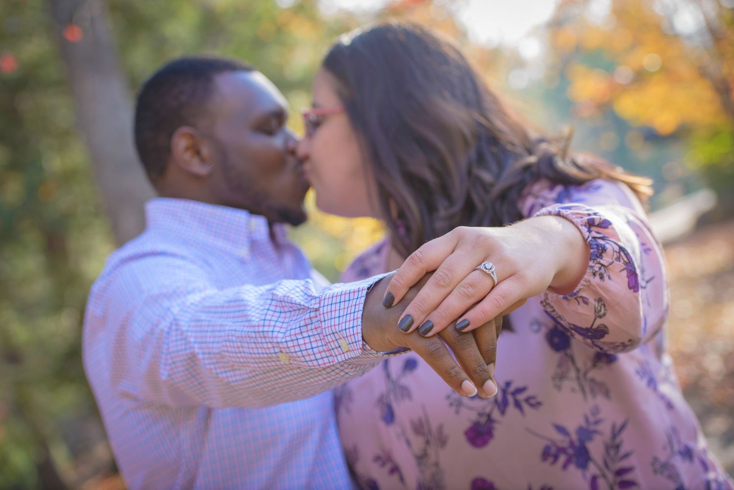 A couple embraces and shares a kiss outdoors during autumn with fall foliage visible in the background by Sevierville TN Photographers.