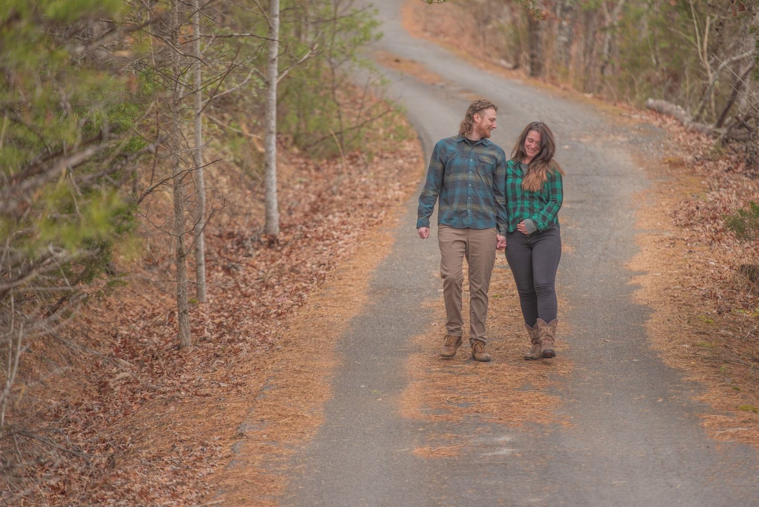A couple walks together on a scenic forest path covered in fallen autumn leaves by Sevierville TN Photographers.